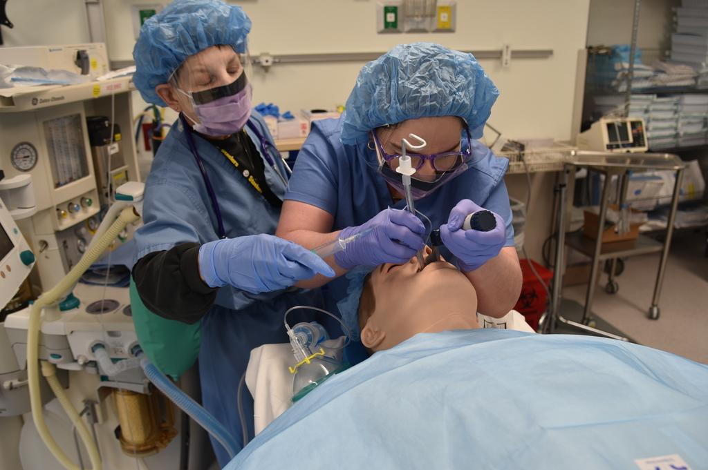 Two people in scrubs in a sim lab practicing anesthesia.
