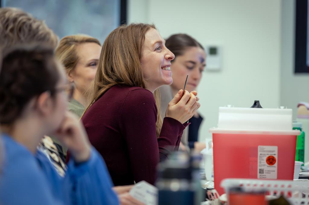 Group of people sitting at a table. The camera is focused on one woman at the table smiling.