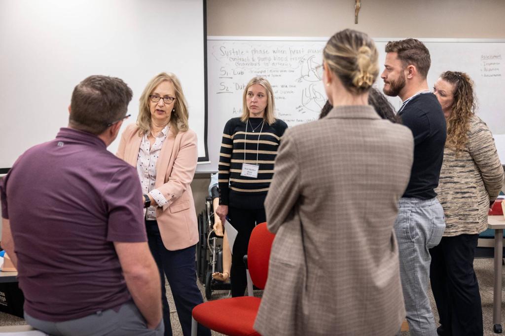 A group of students and a professor engaging in conversation in a classroom setting.