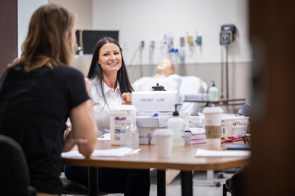 A woman in a clinical setting sitting at a table smiling at someone.