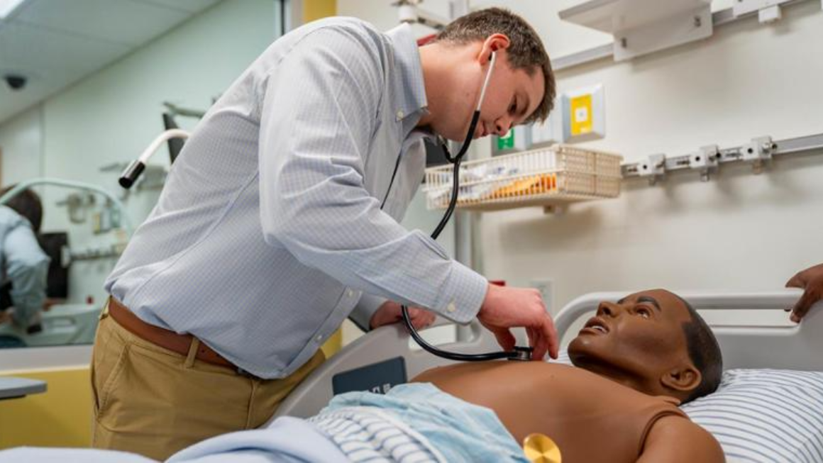 A nursing student using a stethoscope on a mannequin.