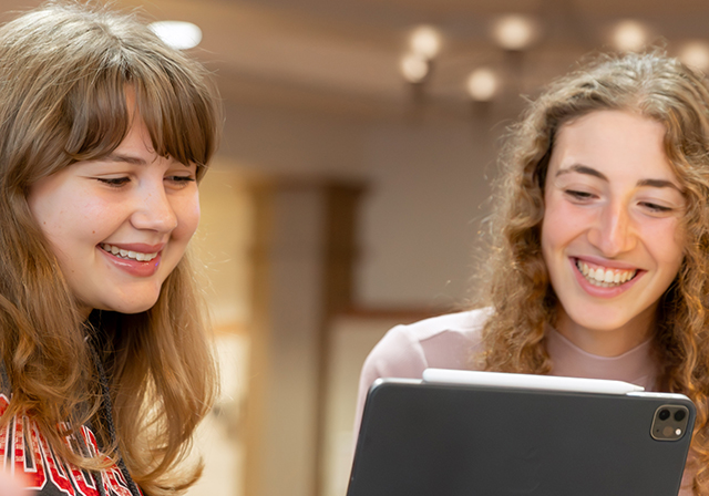 female students taking notes while looking at computer screen, learning online
