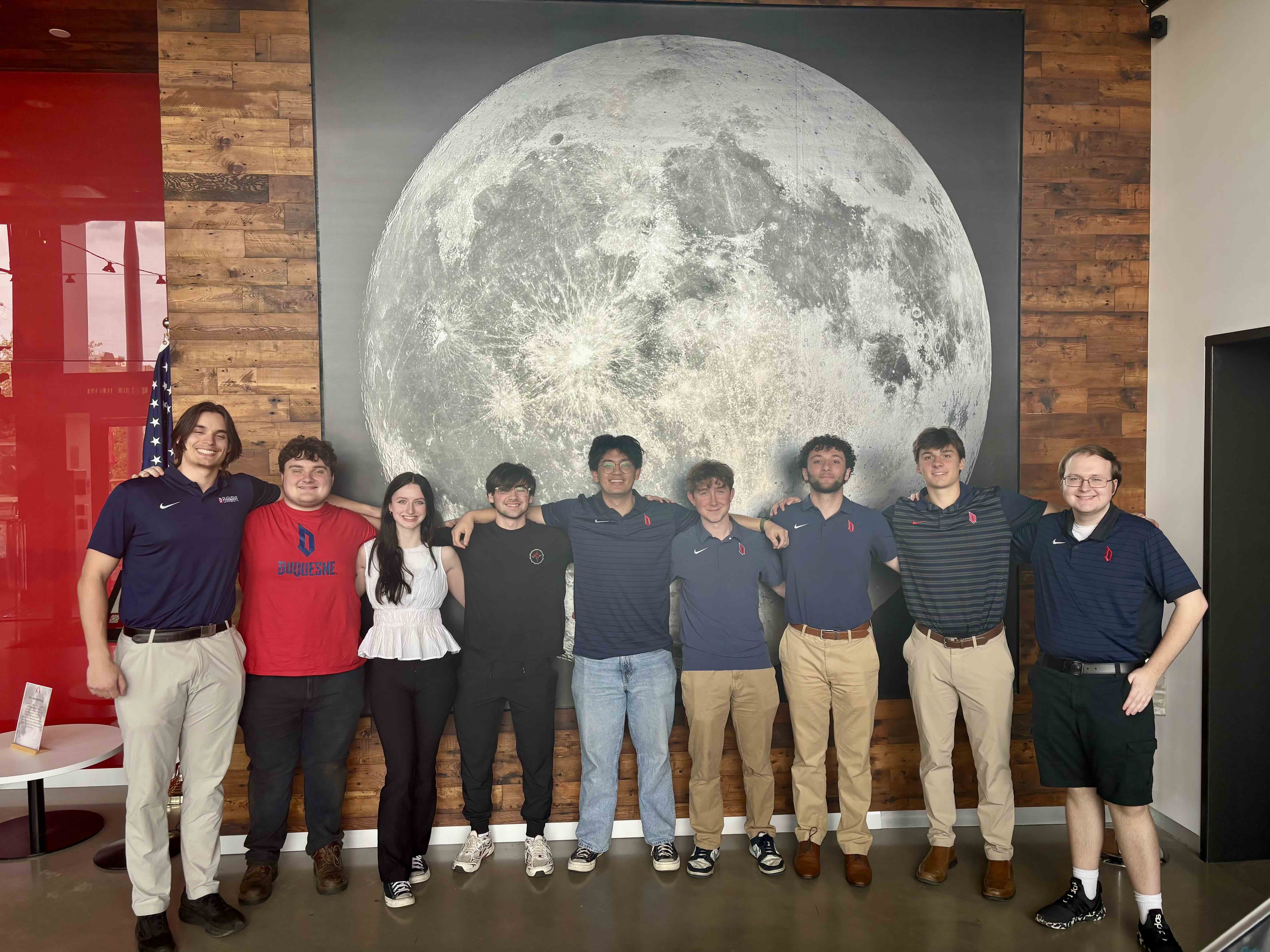 a group of nine students in front of a moon mural