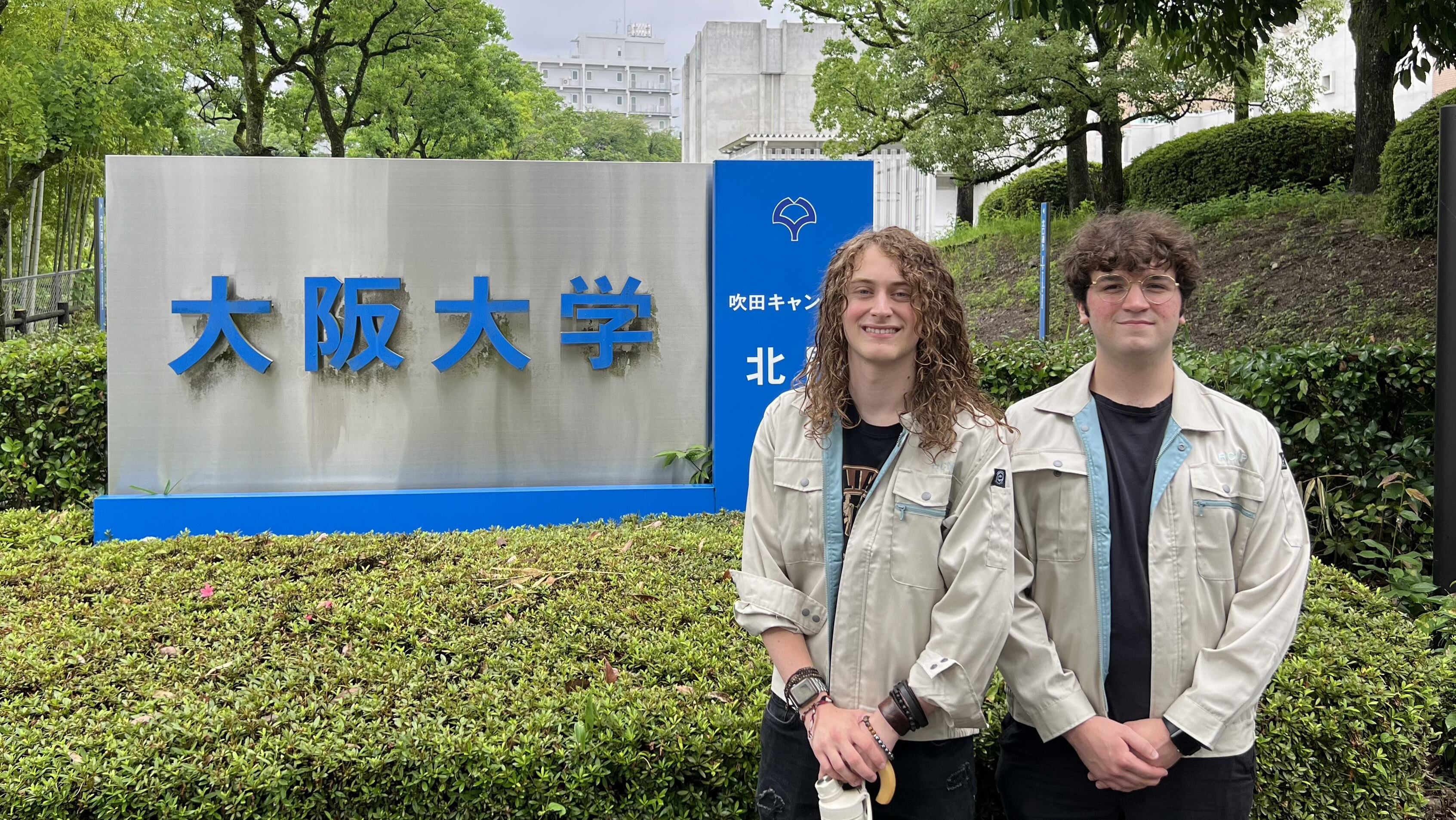 Jacob Dulya and Gabe Pecar post in front of a sign during their summer internship at Osaka University in Japan