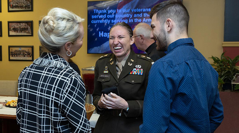 a girl in a military uniform with two people next to her. The girl is laughing