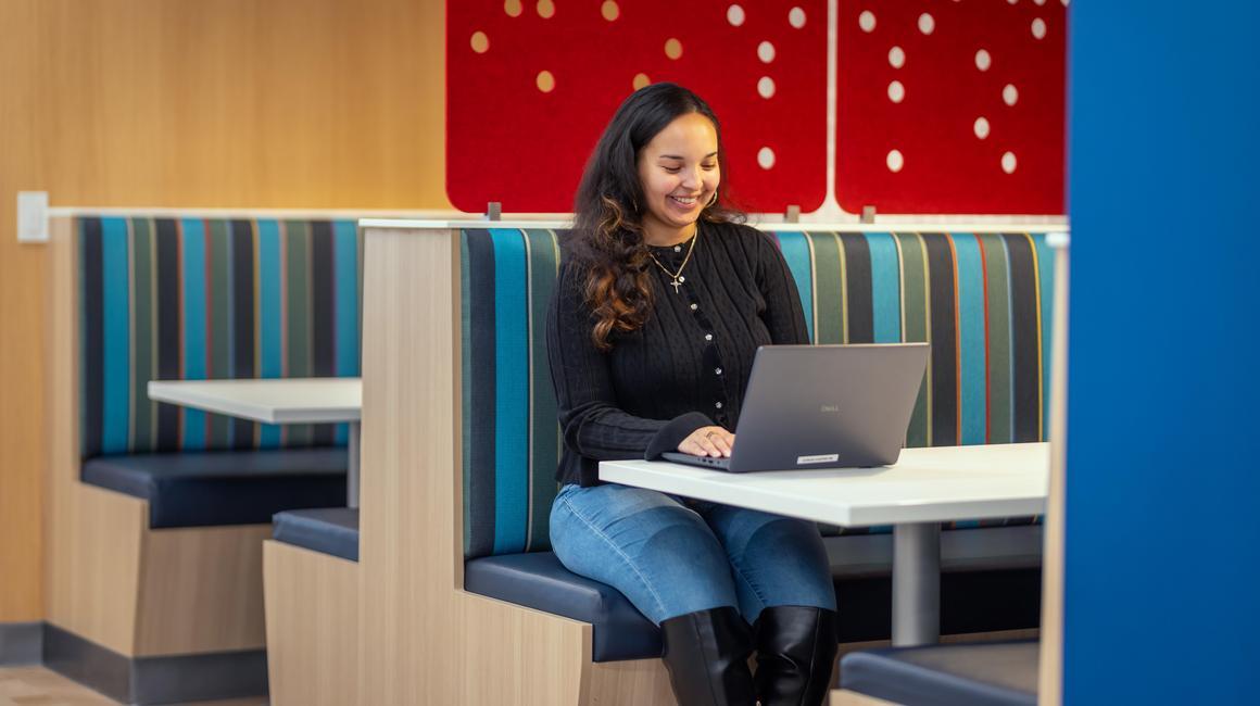 A female students sits in a booth at the Union working on her laptop.