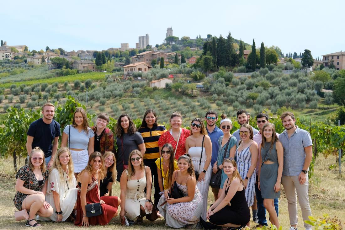 Students in font of rolling, green vineyards of Tuscany.