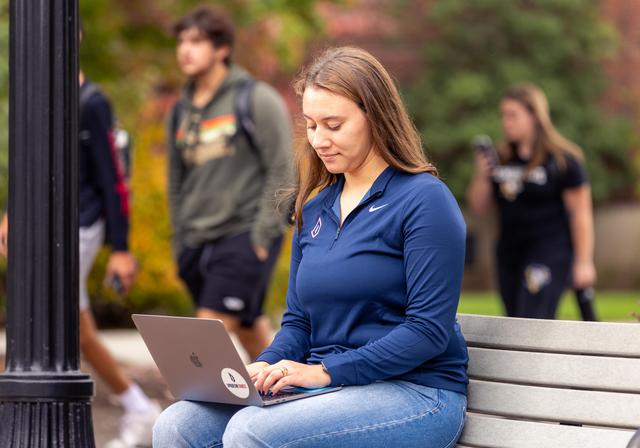 student sitting on bench with computer