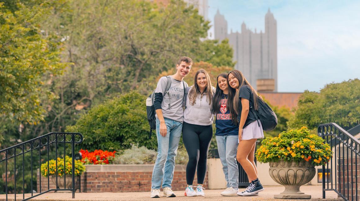 Four DU students outside with Pittsburgh skyline in the background