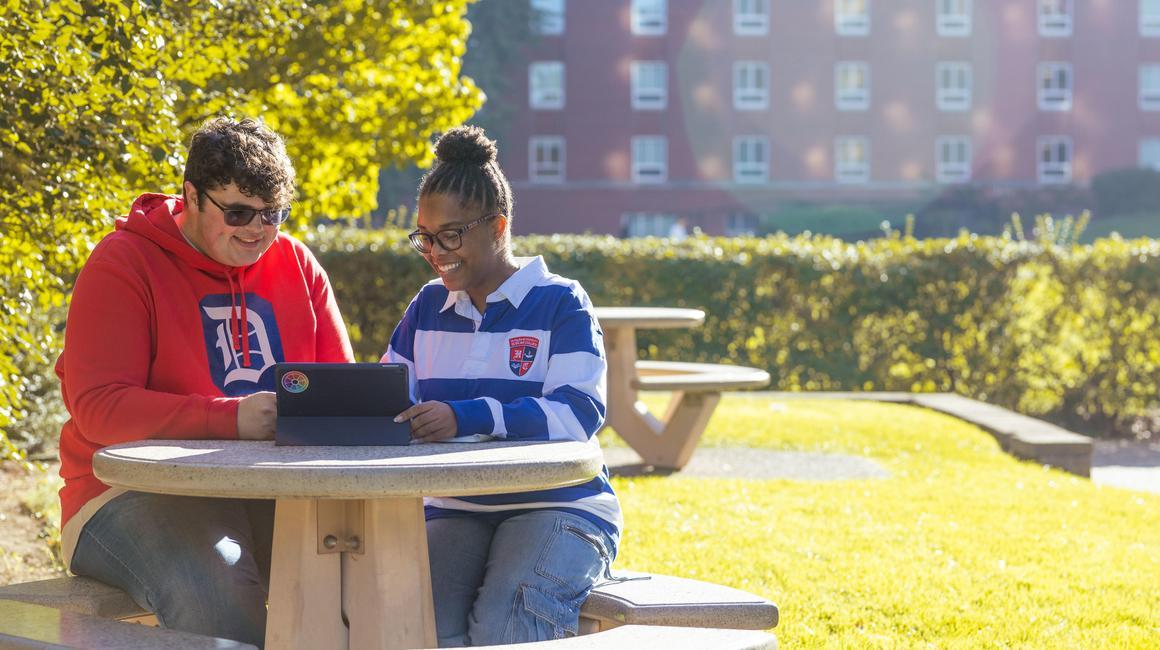 Two Duquesne students sitting at a table outsie of College Hall.