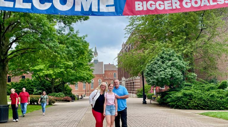 family visiting campus standing under banner that reads ITS TIME FOR BIGGER GOALS