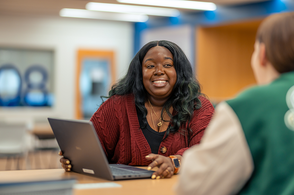 woman speaking with student with her laptop opened in front of her.