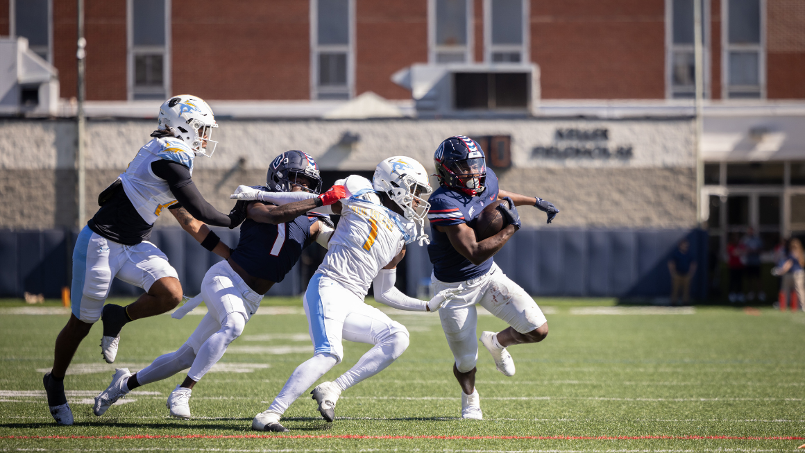 Four football players running, one carries the ball