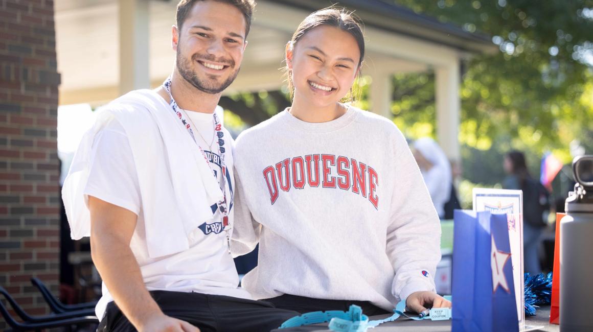 Two Duquesne students standing in front of a table of raffle prizes