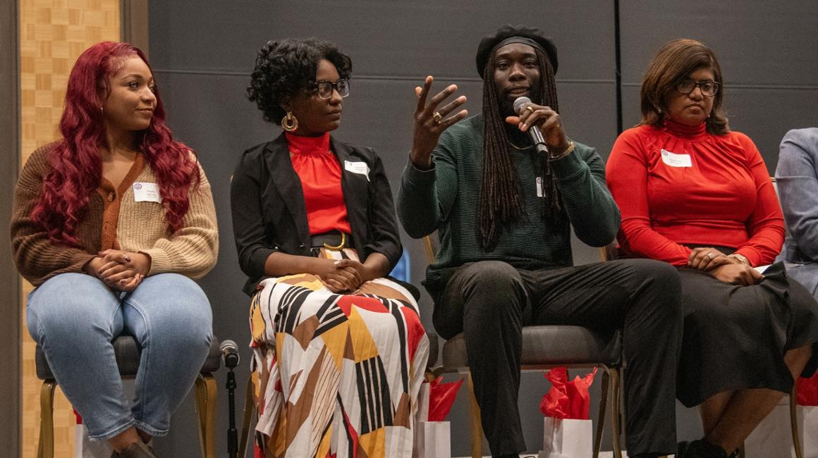 Four people sitting on a stage as part of a panel