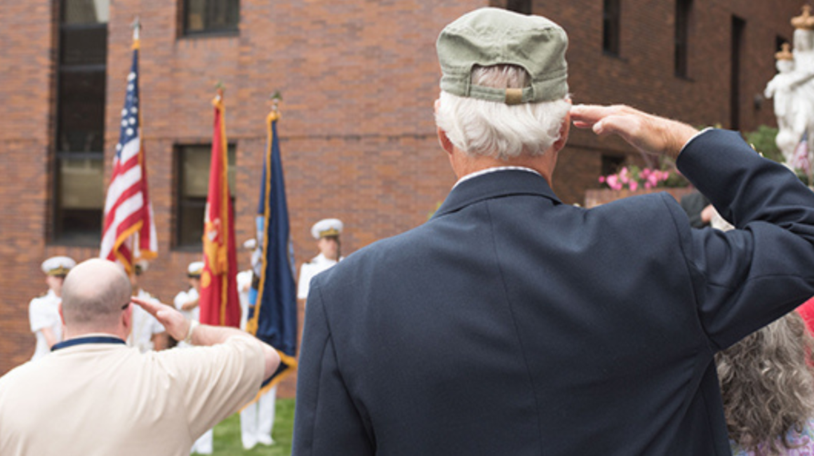 People from behind saluting the American flag