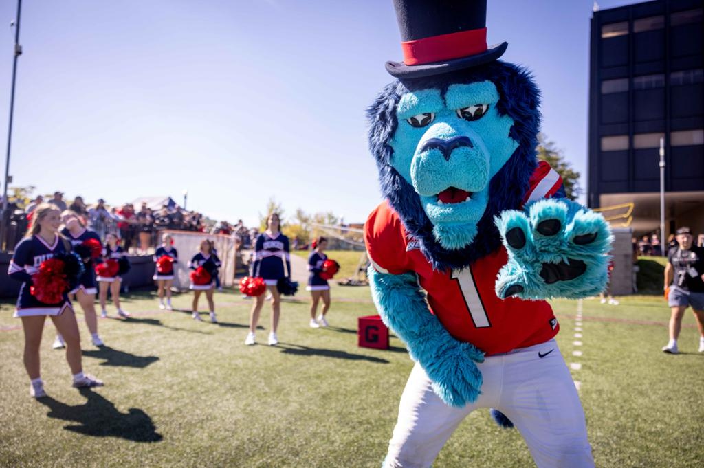 The Duquesne Dukes mascot on a football field with cheerleaders in the background