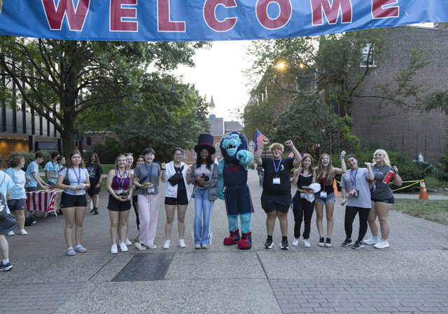 A group of students gather with the Duquesne Duke mascot under the “Welcome” banner on Academic Walk