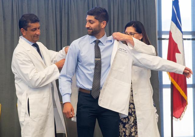 DUQCOM DO student celebrates with his physician-parents as they help with his crisp white coat!