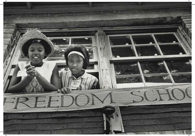 Two young African American female students look out a window with a banner underneath that reads 