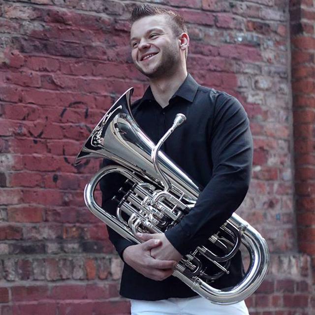 Algirdas Matonis poses with euphonium in front of a brick wall.