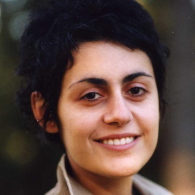 Anoush Tchakarian poses for a headshot in front of a dark, blurry background.