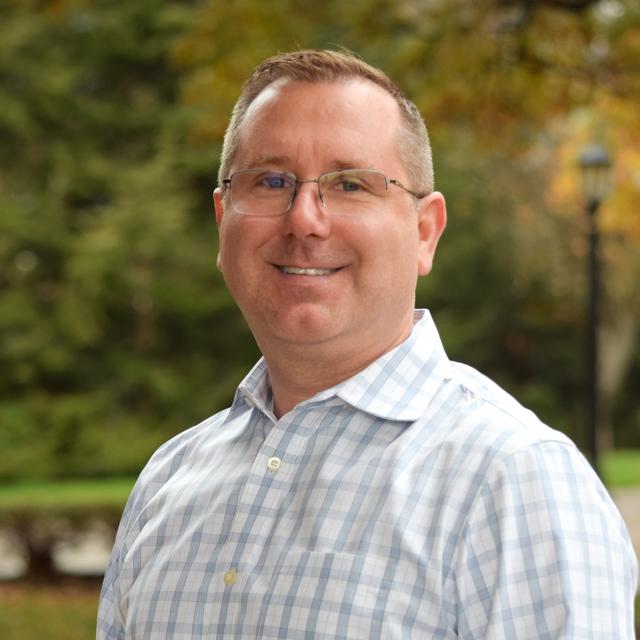 Headshot of Dr. Schmitt with campus tres and lamppost in background