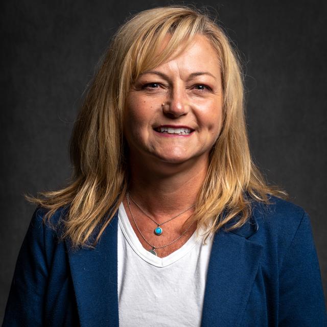 Barb McCandless poses for a headshot in front of a dark gray background.