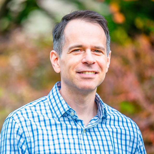 Headshot of Benjamin Binder in front of blurry leaves.