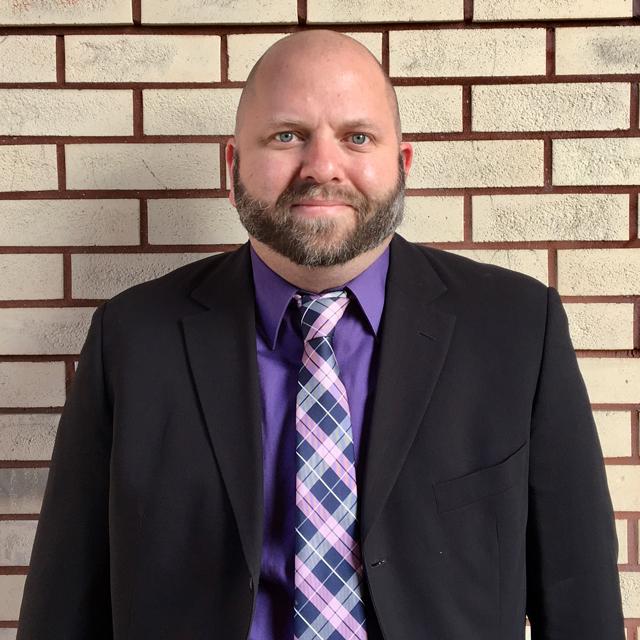 Benjamin Cornelius-Bates poses for a headshot in front of a brick wall.