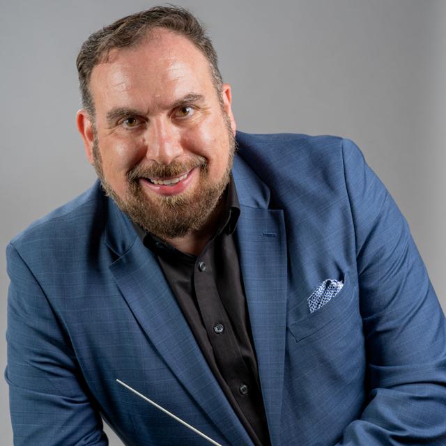 Brian Worsdale holds a conducting baton in a headshot against a gray background.