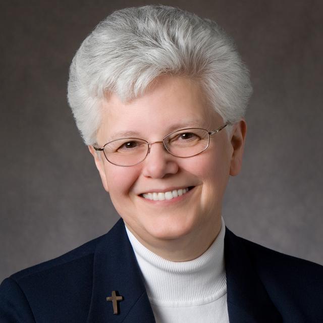Sr. Carole Riley poses for a headshot in front of a gray background.