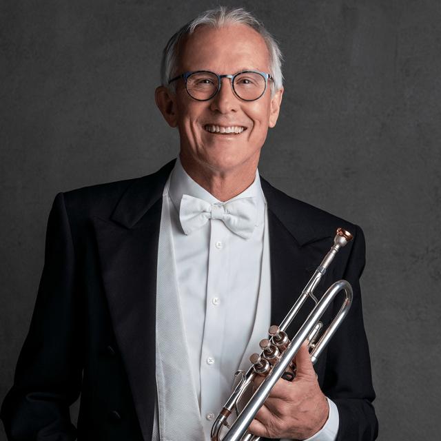 Charles Lirette holds a trumpet for a headshot against a gray background.