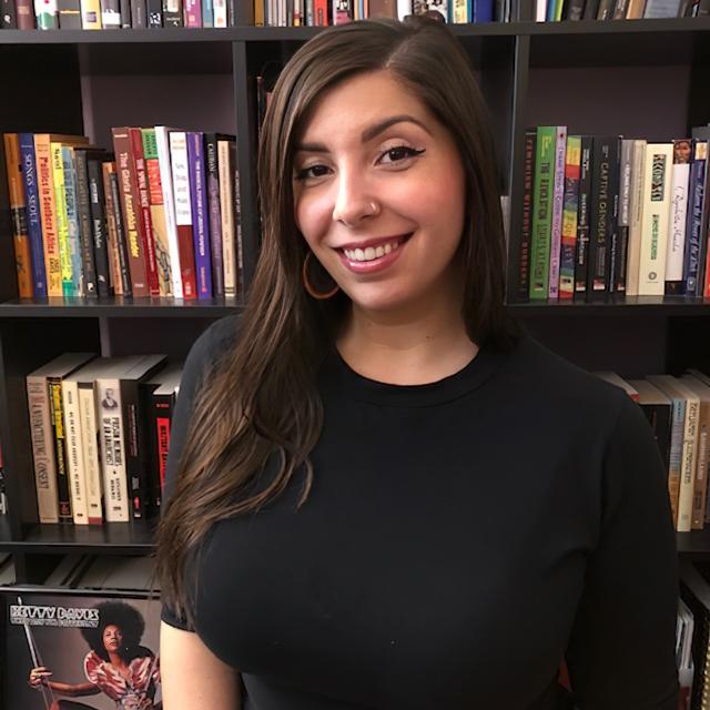 A person poses for a photo in front of a book case.