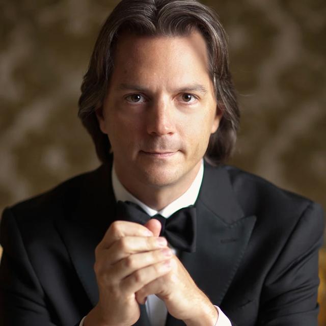 Daniel Meyer in a tuxedo holding a baton.