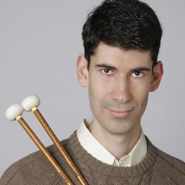 Eliseo Rael holds percussion mallets in front of a gray background.