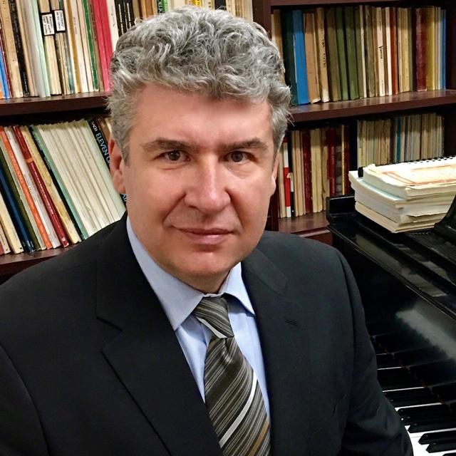Guenko Guechev poses for a headshot in front of a piano and bookshelves.