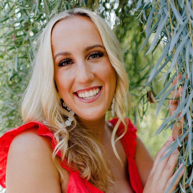 Isabella smiles for a photo next to a tree in a red dress.