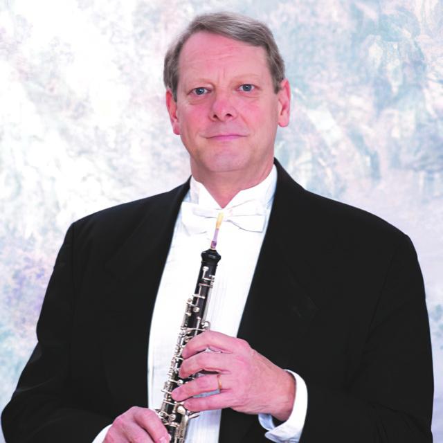 James Gorton wears a tuxedo and holds an oboe.