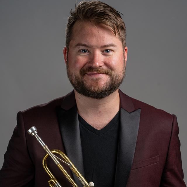 J.D. Chaisson holds a trumpet in front of a gray background.