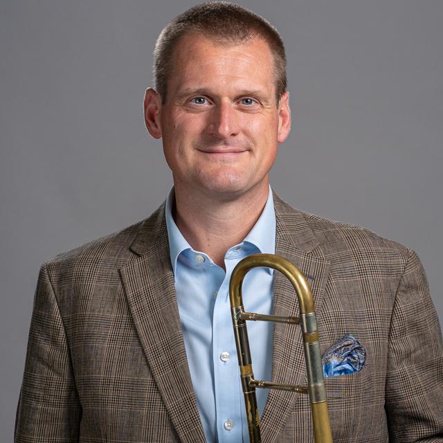 Jeff Bush poses with trombone in front of a gray background.