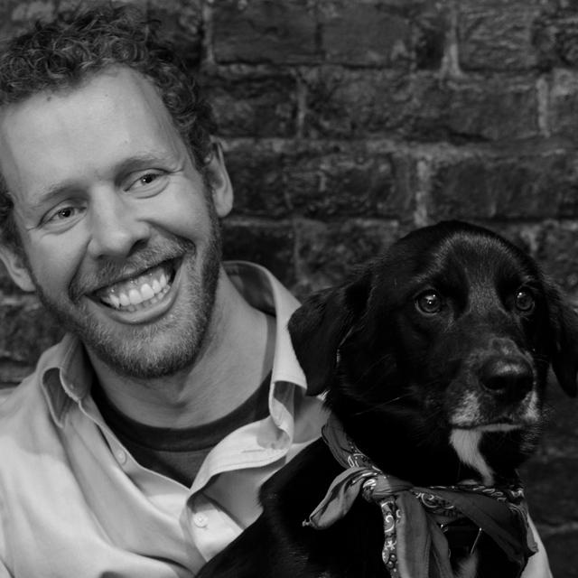 Jesse Naus poses with dog in front of brick wall. 