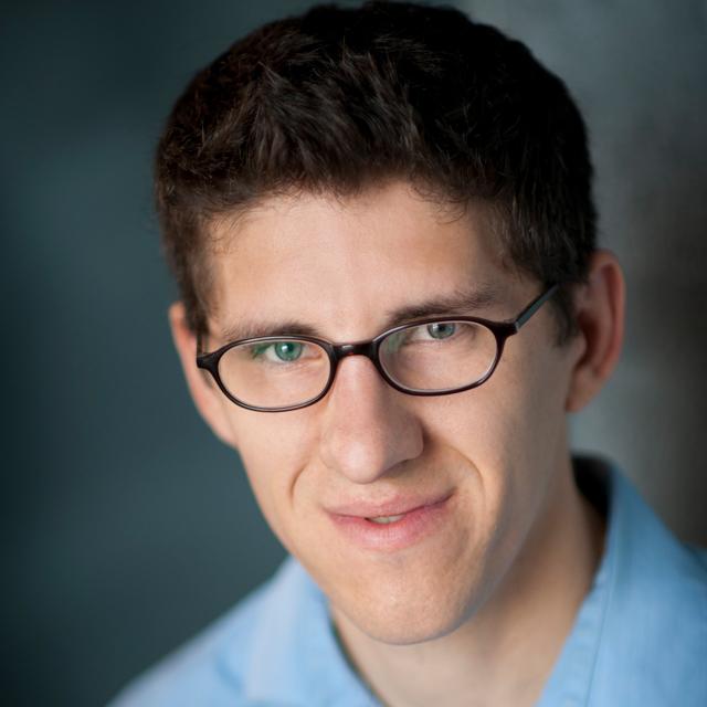 Joseph Sheehan poses for a headshot in front of a blue background.