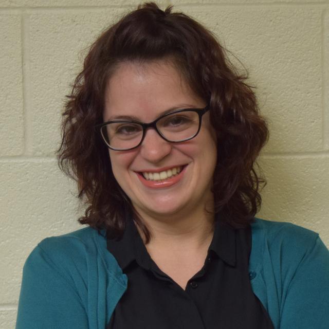 Johnna Mernick poses for a headshot against a beige wall.