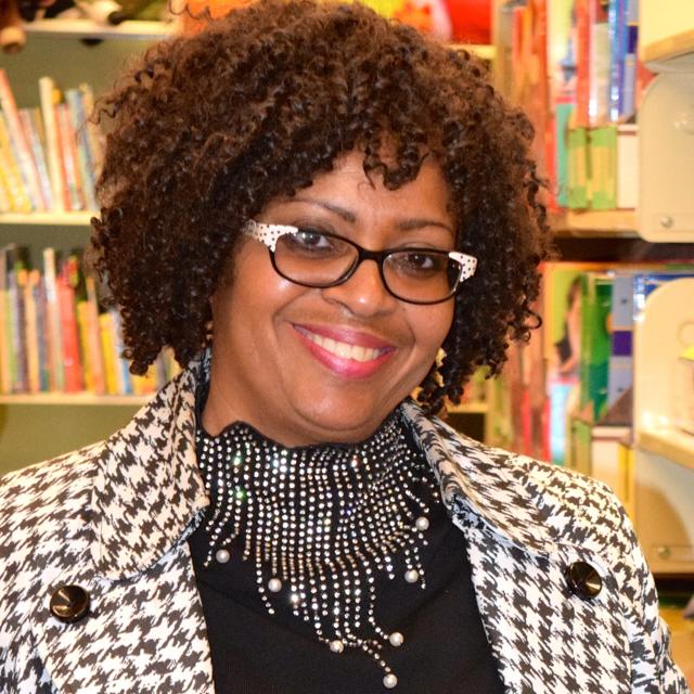 Headshot of Dr. Julia Williams with library's Curriculum Center in background with colorful bookshelves
