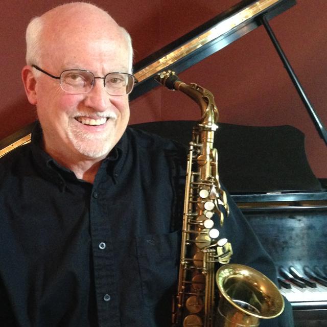 Keith Young holds a saxophone in front of a piano.