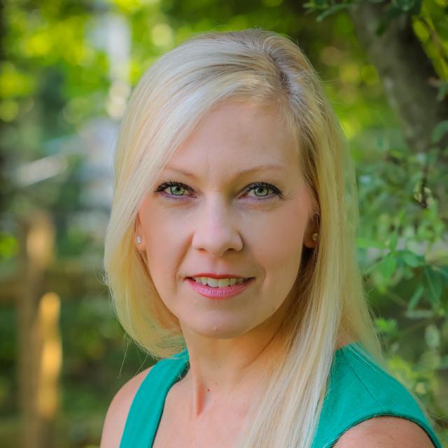 Kelley Krepin DeFade poses for a headshot against a blurry outdoor background.