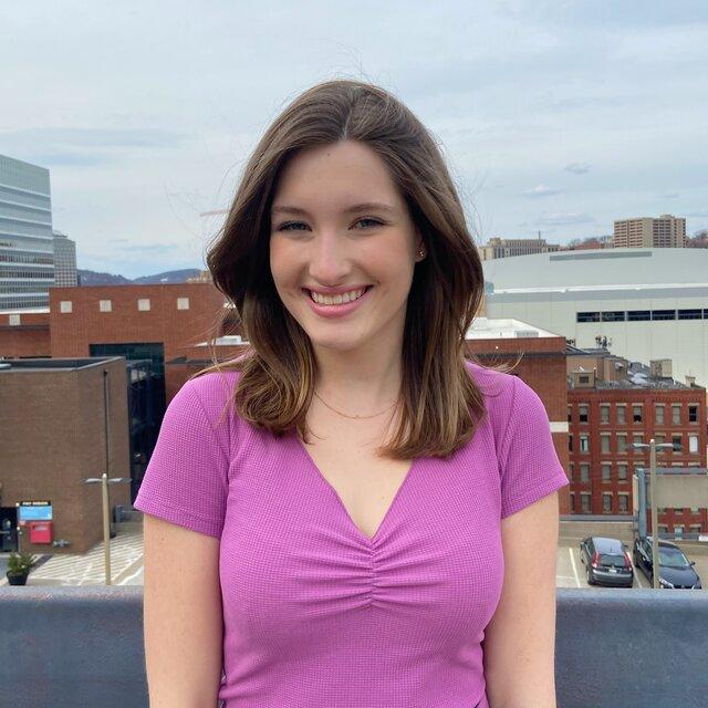 Lauren smiles in a purple shirt in front of Duquesne's skyline.