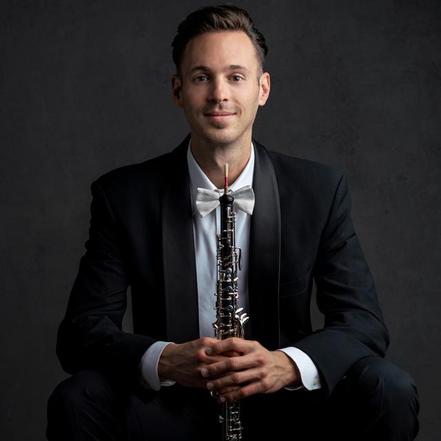 Max Blair wears a tuxedo and holds an oboe.