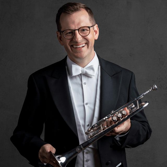 Micah Wilkinson wears a tuxedo and holds a trumpet.